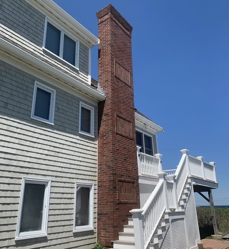Tall red-brick chimney against a clear sky beside gray shingle siding