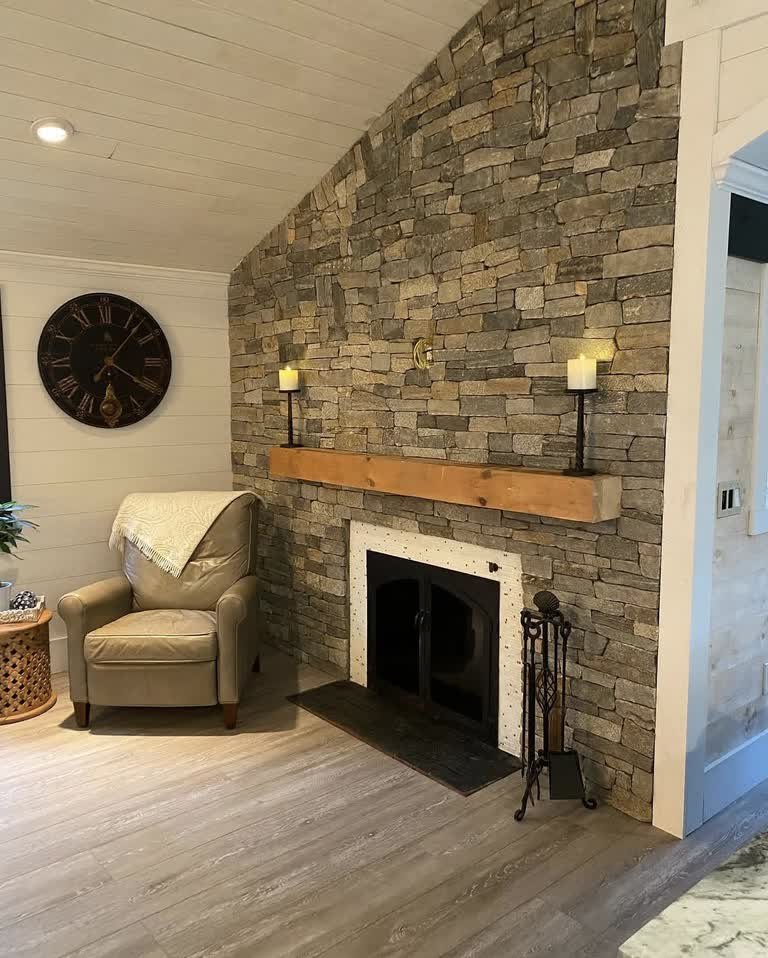 Floor-to-ceiling ledgestone fireplace with a wood mantel in a living space