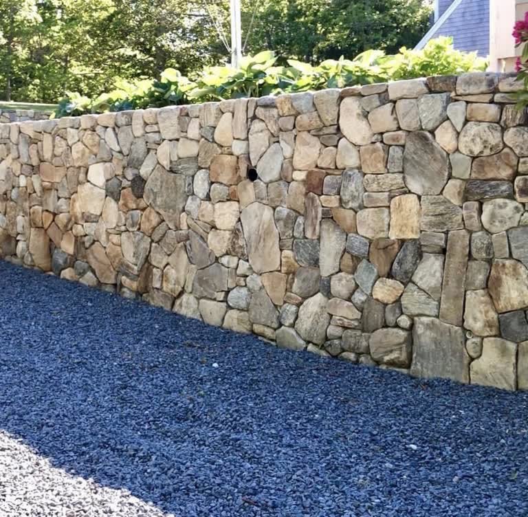 Long natural-stone retaining wall beside a dark gravel drive