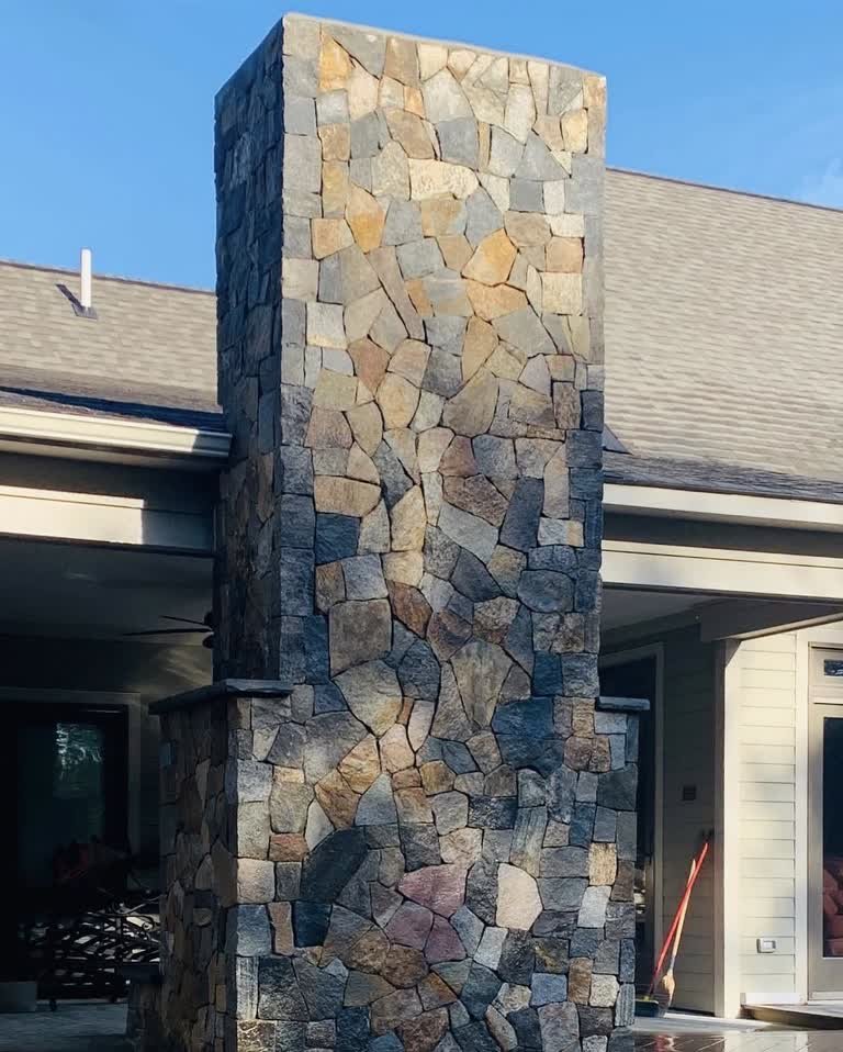 Tall stone-clad chimney rising above a covered outdoor space