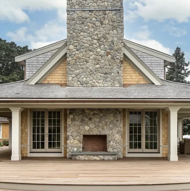 Stone fireplace and chimney centered on a shingled covered porch