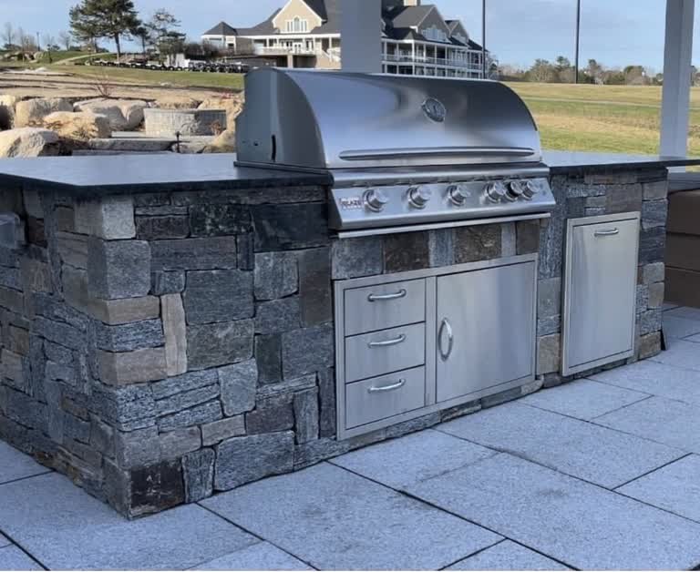 Stone-clad outdoor kitchen with a stainless-steel grill and dark countertop