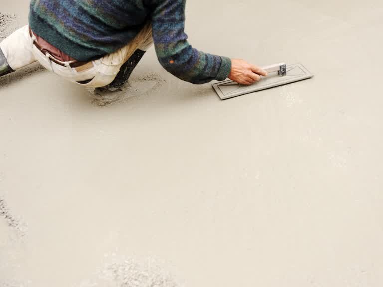 Representative stock photograph of a worker smoothing freshly placed concrete with a hand float